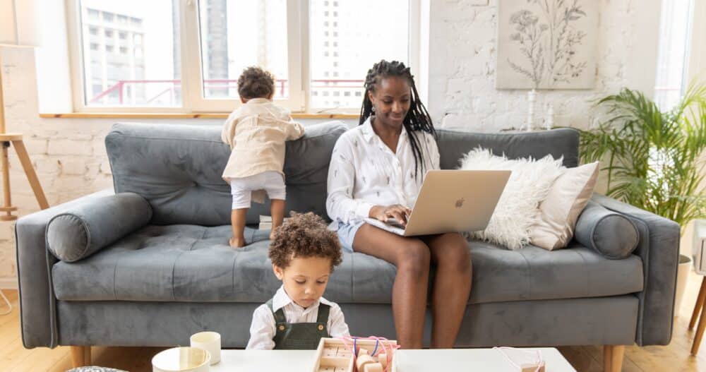 Woman working from home on the couch while her young children play nearby