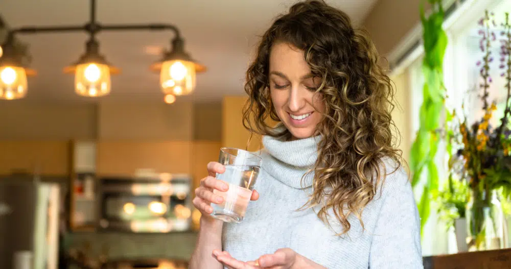 Woman smiling holding a glass of water about to take her medication for her mental health
