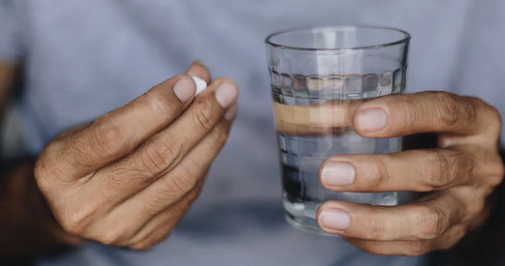 A pair of hands, one holding mental health medication and the other holding a glass of water