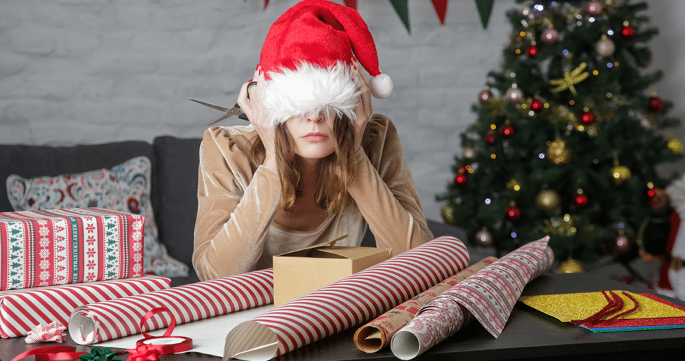 Stresses woman in santa hat wrapping presents.