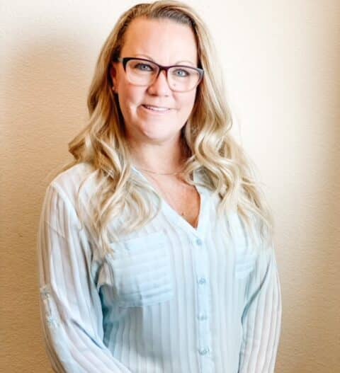 Headshot of Connie Fielder, MFT-I, dressed in a white striped button up blouse with dark rimmed eyeglasses.