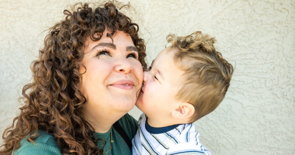 A woman in a green shirt standing outside and holding her infant son