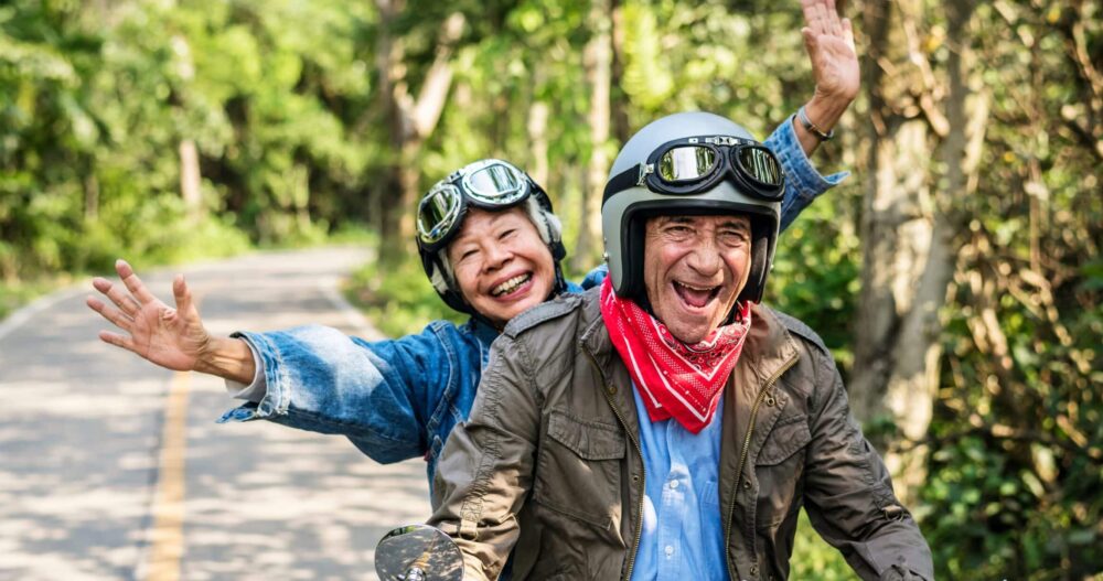 Older couple on a moped driving down the road and smiling