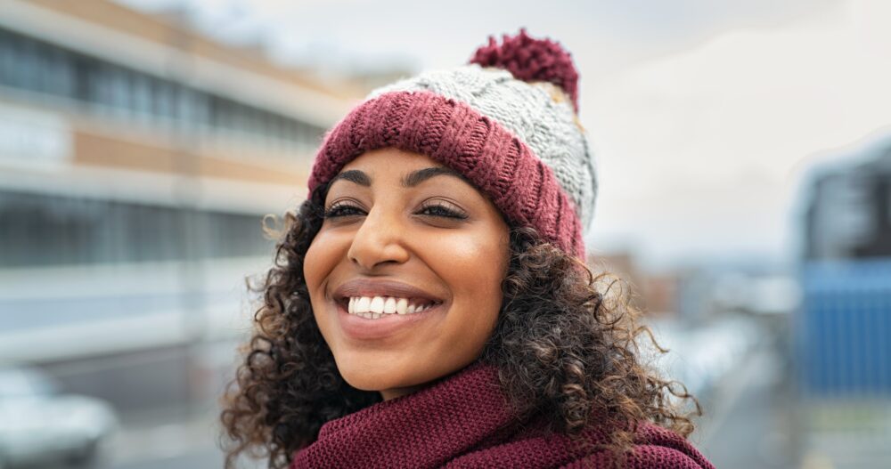 Closeup face of young happy woman enjoying winter, wearing scarf and woolen cap.