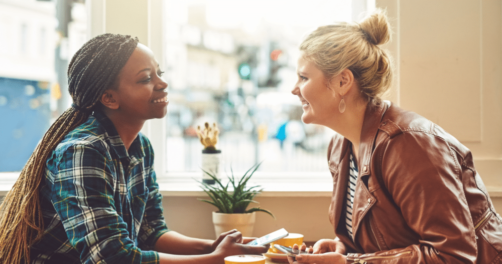 Two women sitting across from each other in a coffee shop. They are smiling and having a conversation