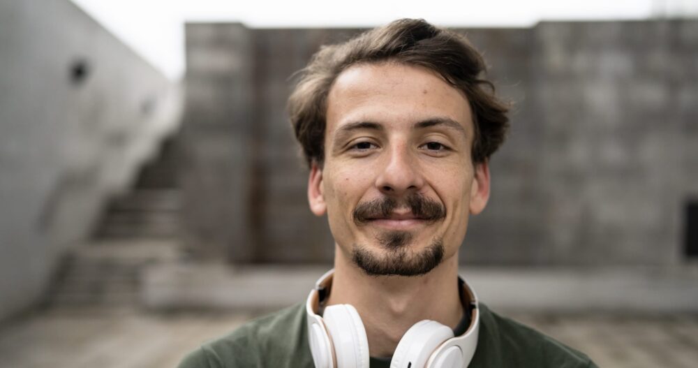 A man in a green shirt with white headphones around his neck smiling for the camera