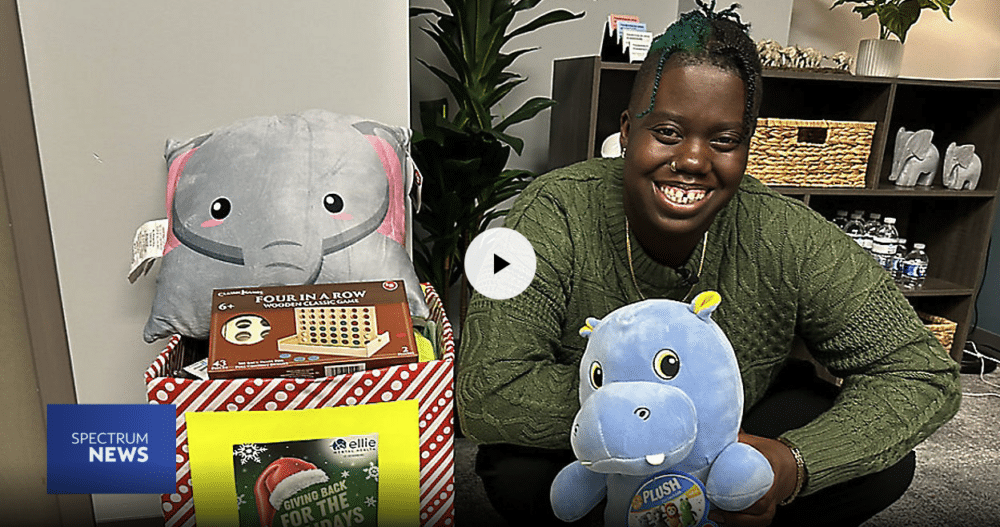 Dominique Mickler, a Therapist at our Ellie Mental Health St. Petersburg, FL Clinic standing in her office and holding a bunch of toys for her toy drive