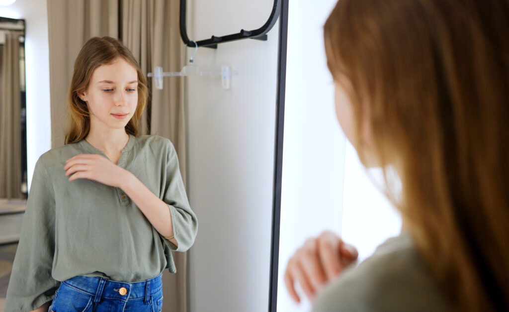 Teen girl standing in the mirror fixing her shirt collar