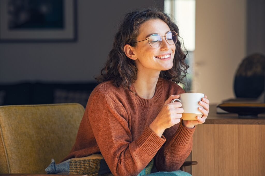 HAppy young woman sitting on the couch drinking coffee after getting therapy for depression