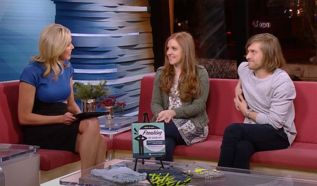 Ellie Mental Health founders Erin Pash and Kyle Keller sitting on a red couch being interviewed by a woman with blond hair wearing a black shirt and blue top about Erin Pash's book, How to Stop Freaking the %#$! Out! (For Couples)