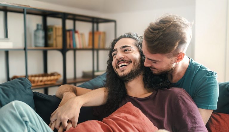 Heartwarming scene of two young gay men laughing and embracing on a sofa, showcasing love and affection.