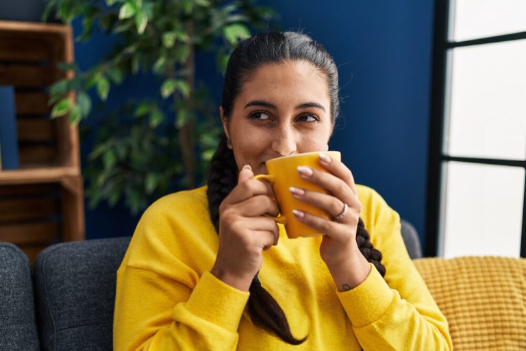 Young woman drinking coffee sitting on sofa at home