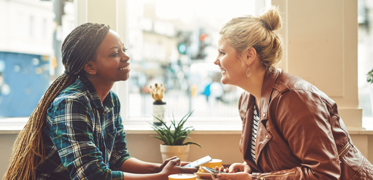 Two women sitting across from each other in a coffee shop. They are smiling and having a conversation