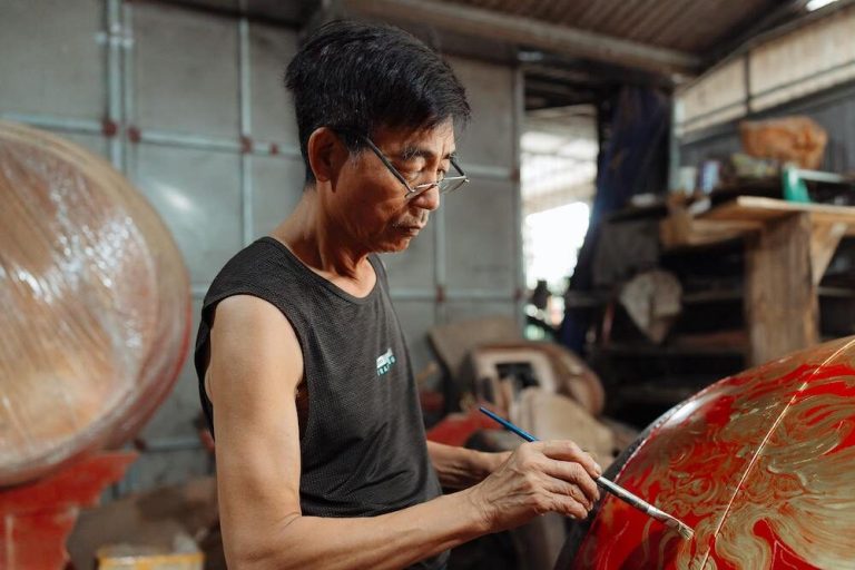 Man in a workshop painting a dragon on a drum
