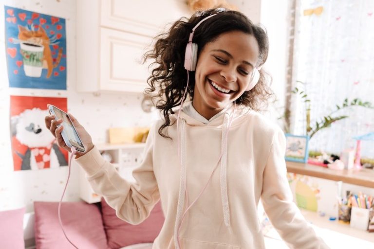 Happy teen in headphones listening to music and dancing in her cozy room at home