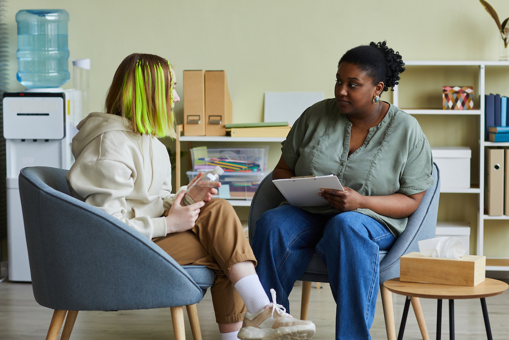 Social worker talking to teenage girl while they sitting on armchairs at office
