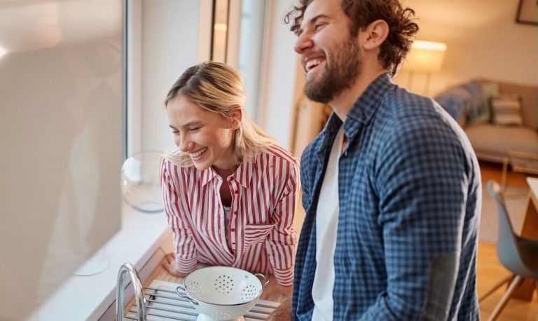 Man and woman laughing with each other while doing dishes
