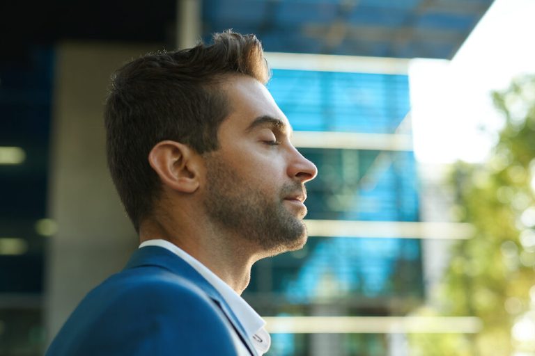 Young businessman standing with his eyes closed and taking a deep breath outside during a break from work