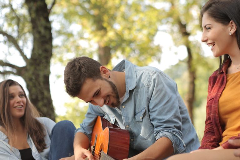Man playing the guitar with some friends outside camping
