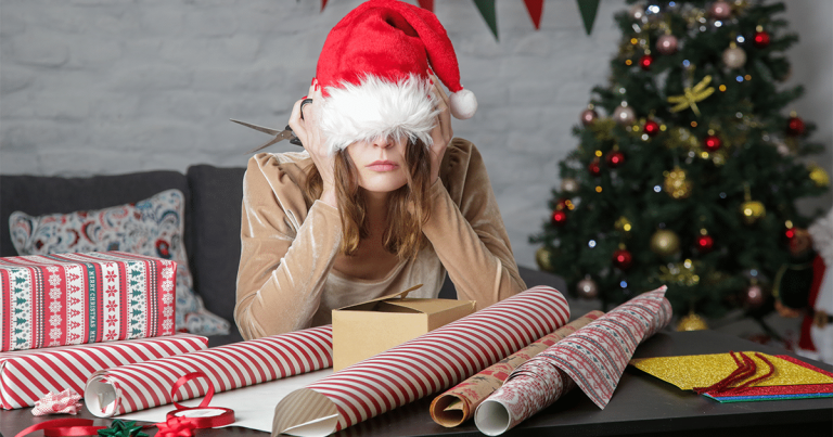 Stresses woman in santa hat wrapping presents.