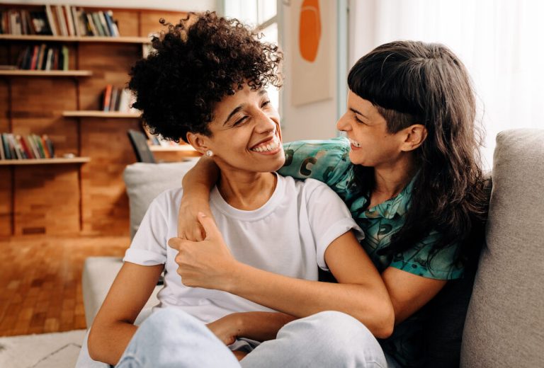 Happy young lesbian couple sharing a laugh while sitting together in their living room.