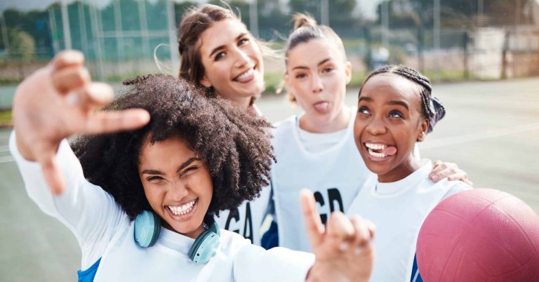 A group of girls holding a dodgeball pn thw blacktiop at recess. They are looking at the camera and smiling
