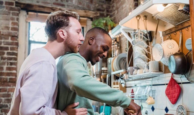 Two men hugging and smiling while cooking dinner