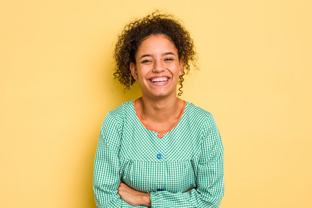 Teacher standing in front of a yellow wall laughing