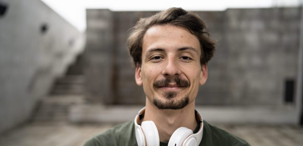 A man in a green shirt with white headphones around his neck smiling for the camera