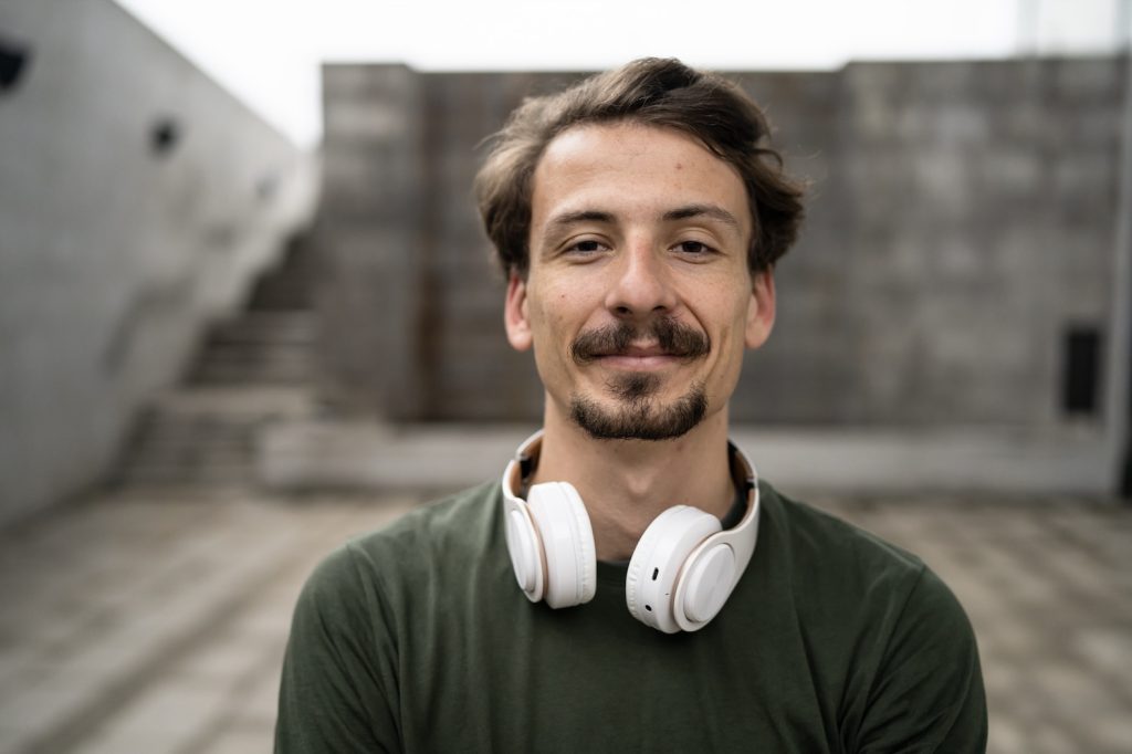 A man in a green shirt with white headphones around his neck smiling for the camera