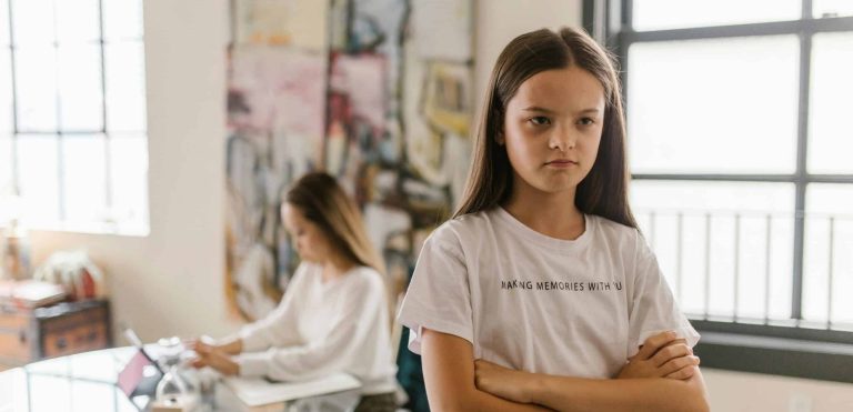 Girl facing away from her mom with her arms crossed and an angry look on her face