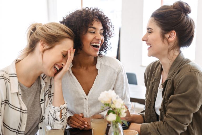 Three women sitting at a table in a coffee shop laughing together.