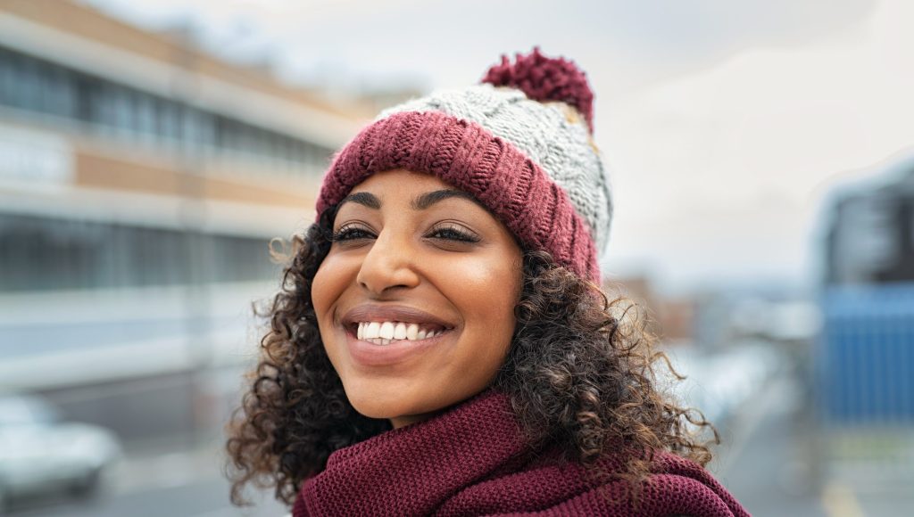 Closeup face of young happy woman enjoying winter, wearing scarf and woolen cap.
