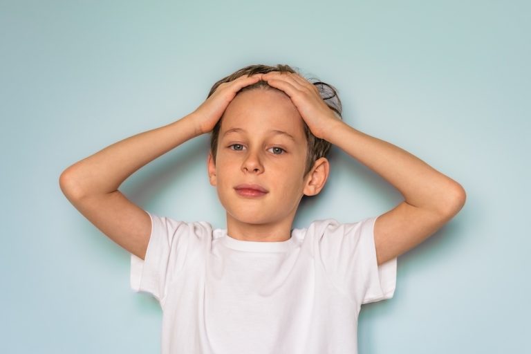 Portrait of a boy in a white t-shirt. The child folded his hands on his head and looks directly into the camera