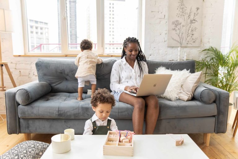 Woman working from home on the couch while her young children play nearby