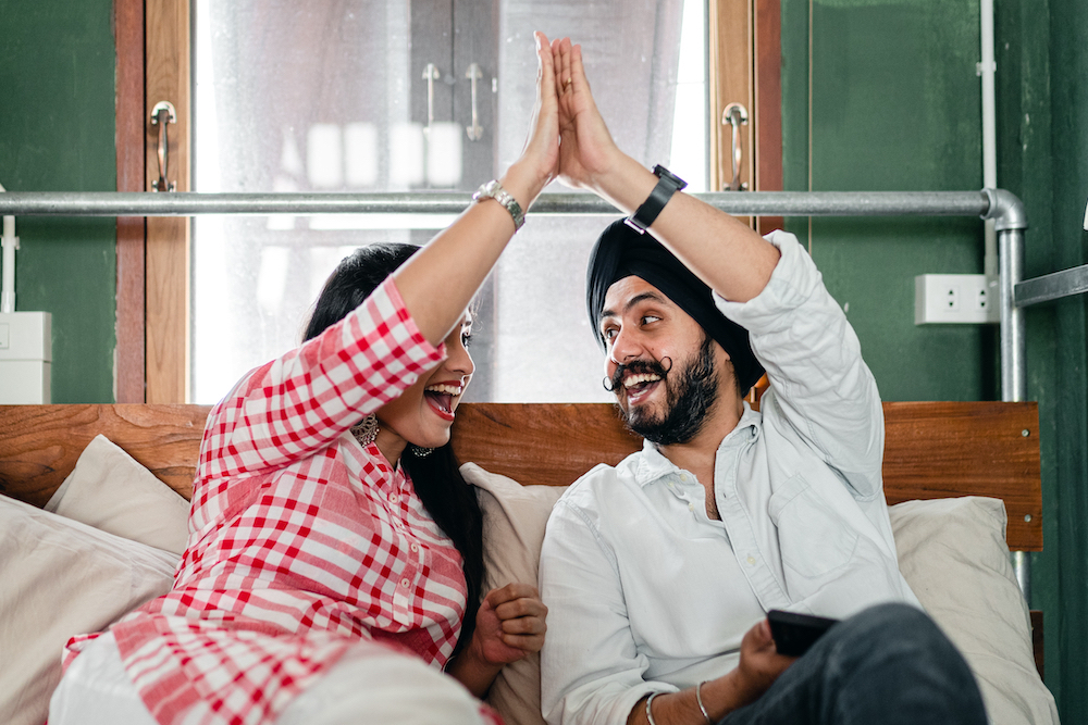 A couple sitting on a couch high fiving each other