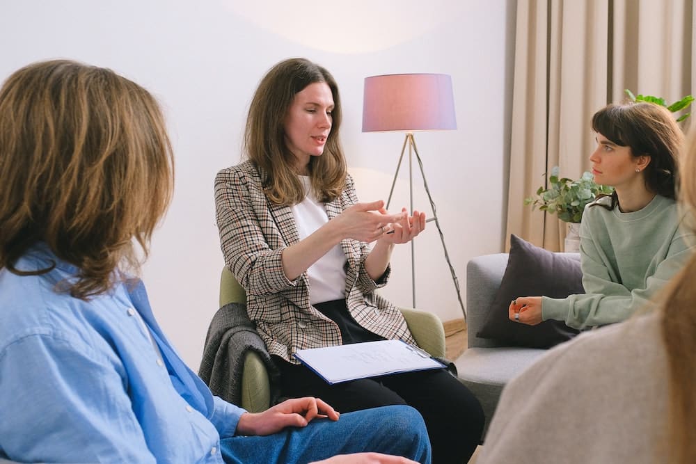 A group of women sitting with a therapist who is talking to them and taking notes