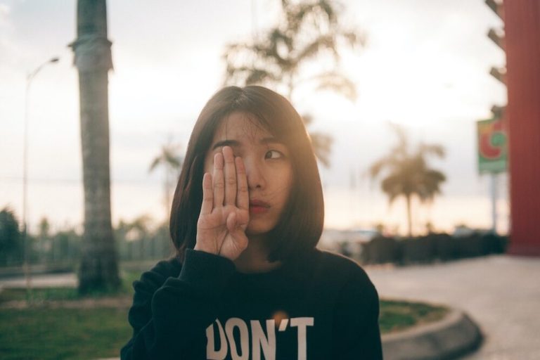 Woman standing outside covering one of her eyes with her hand