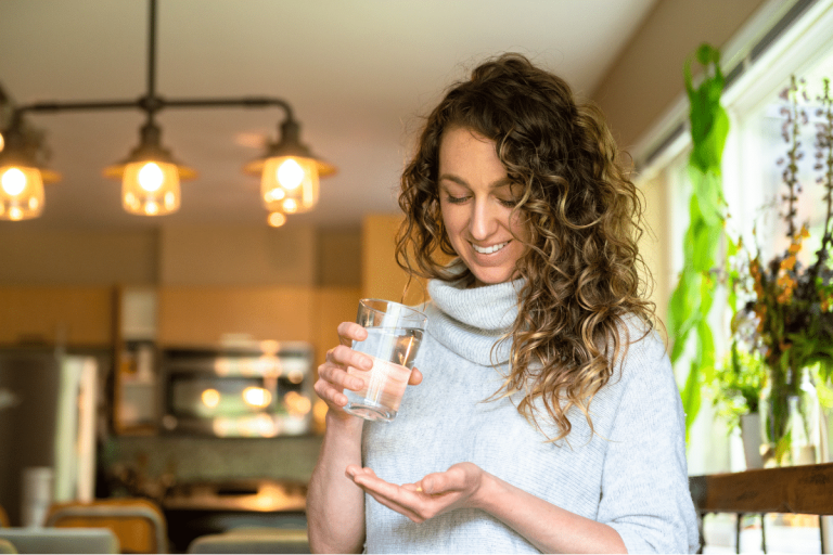 Woman smiling holding a glass of water about to take her medication for her mental health