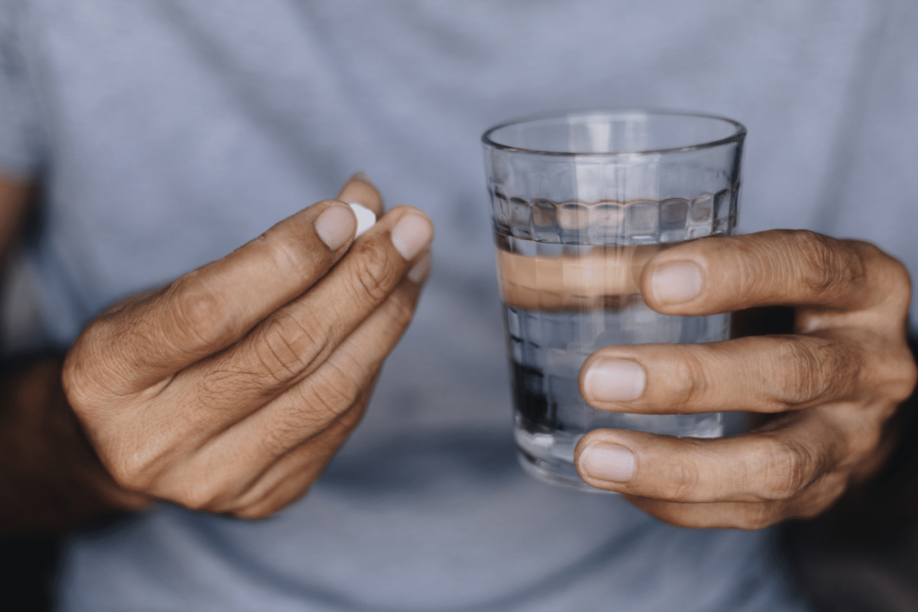 A pair of hands, one holding mental health medication and the other holding a glass of water