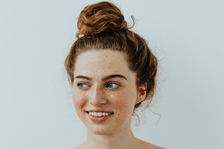 Girl with freckles is looking away and smiling, on a white background
