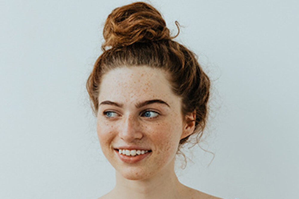 Girl with freckles is looking away and smiling, on a white background
