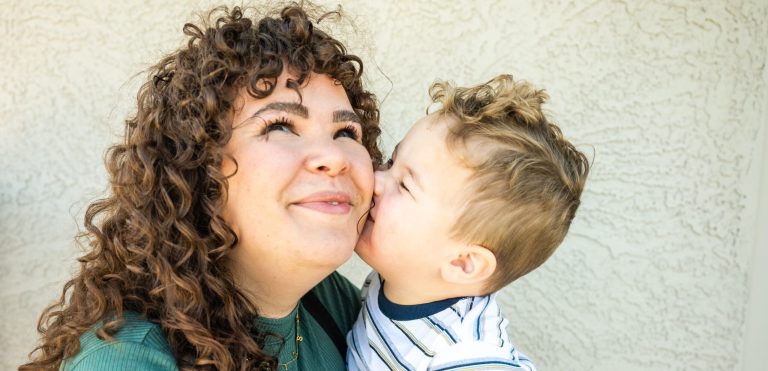 A woman in a green shirt standing outside and holding her infant son
