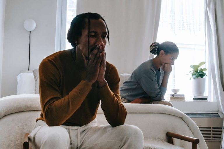 Man sitting at end of bed covering his mouth with his hands deep in thought