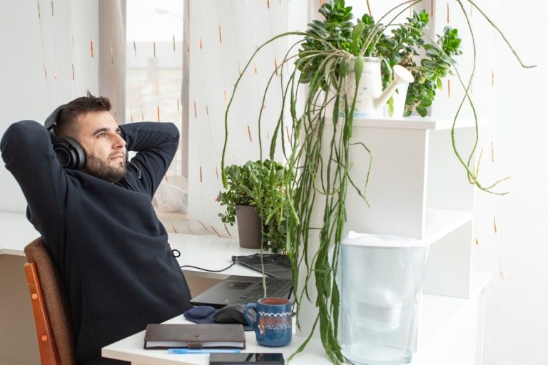 Man in office quiet quitting in the workplace and wearing headphones in relaxed position