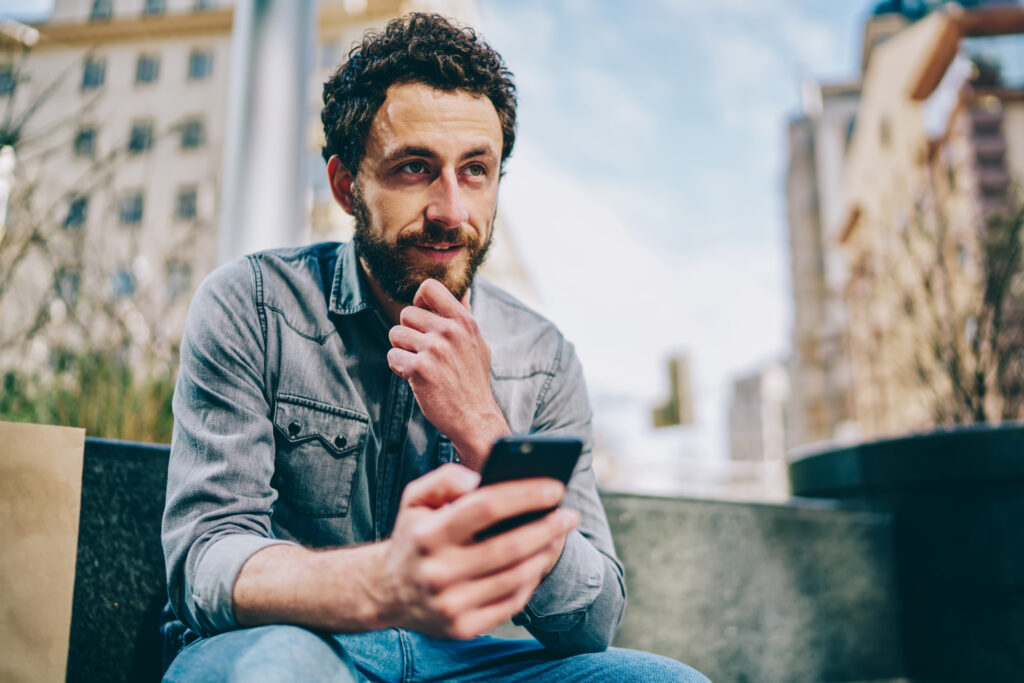 Man with a beard sitting outside looking at jis phone