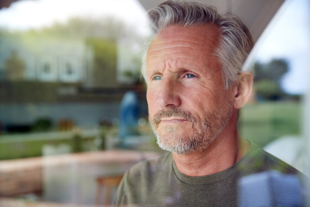 Older man standing in his house looking out the window