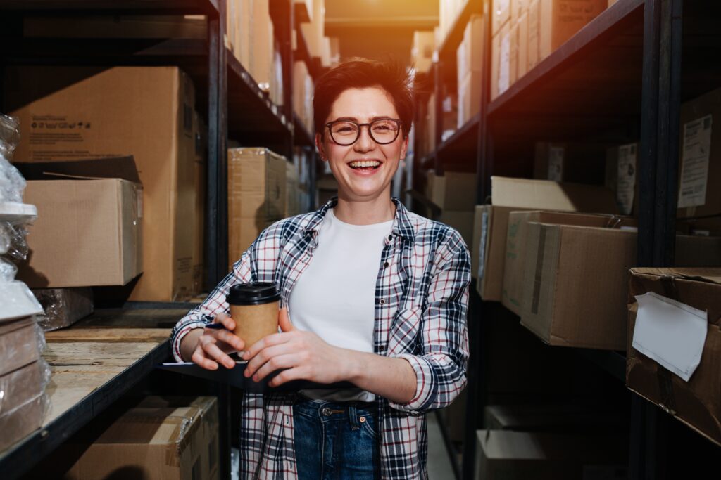 Person with short hair standing in a warehouse holding coffee