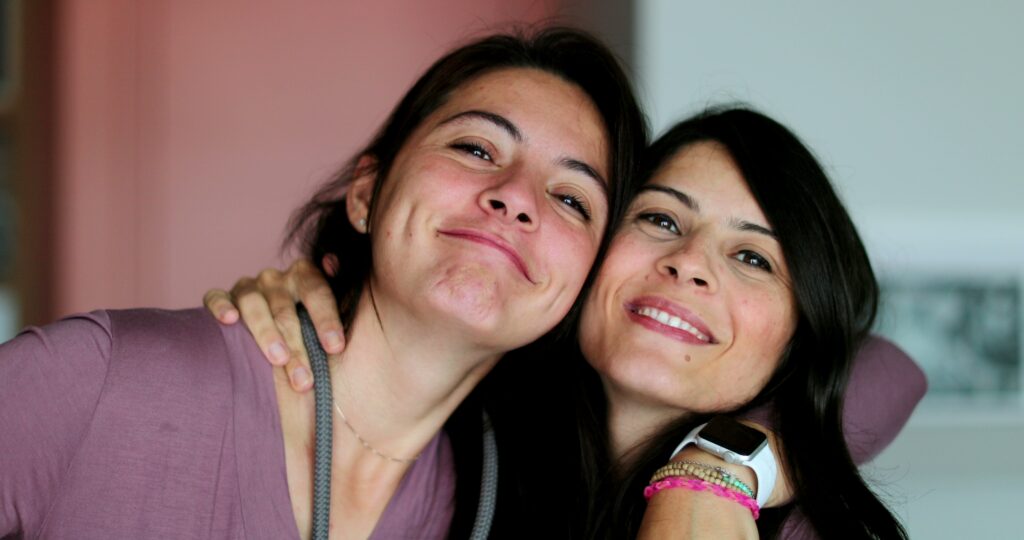 Swo women with their arms around each others shoulders smiling