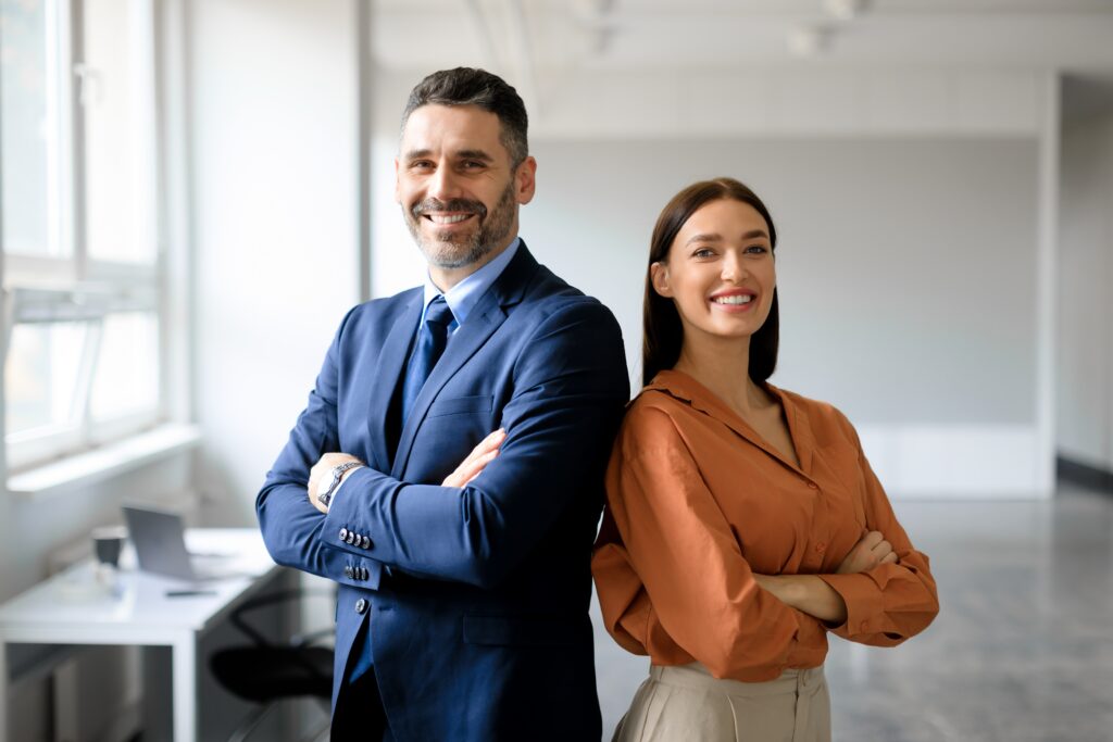 A man in a woman in professional clothing smiling while standing back to back